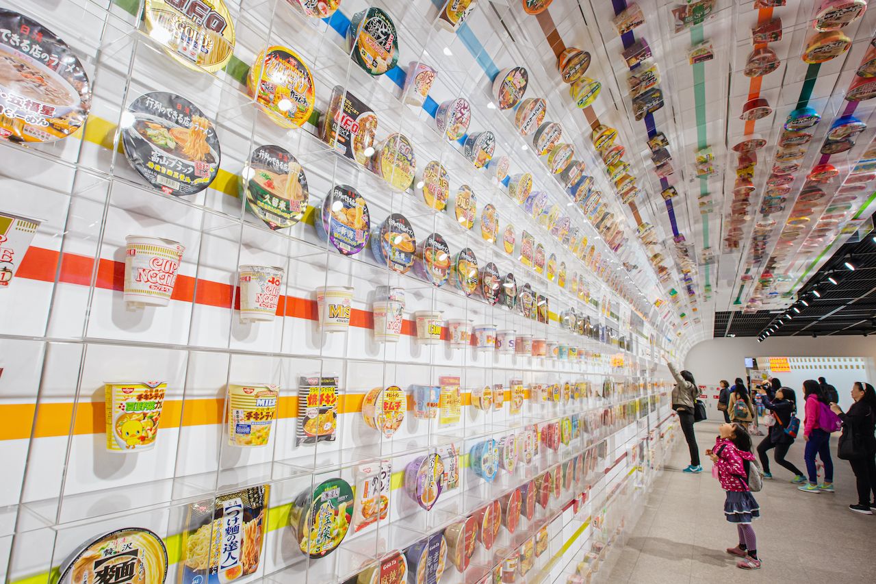 Little girl look up many cup noodles decoration on wall exhibition tell story about instant noodles at The Cup Noodles Museum Osaka., museums in Japan